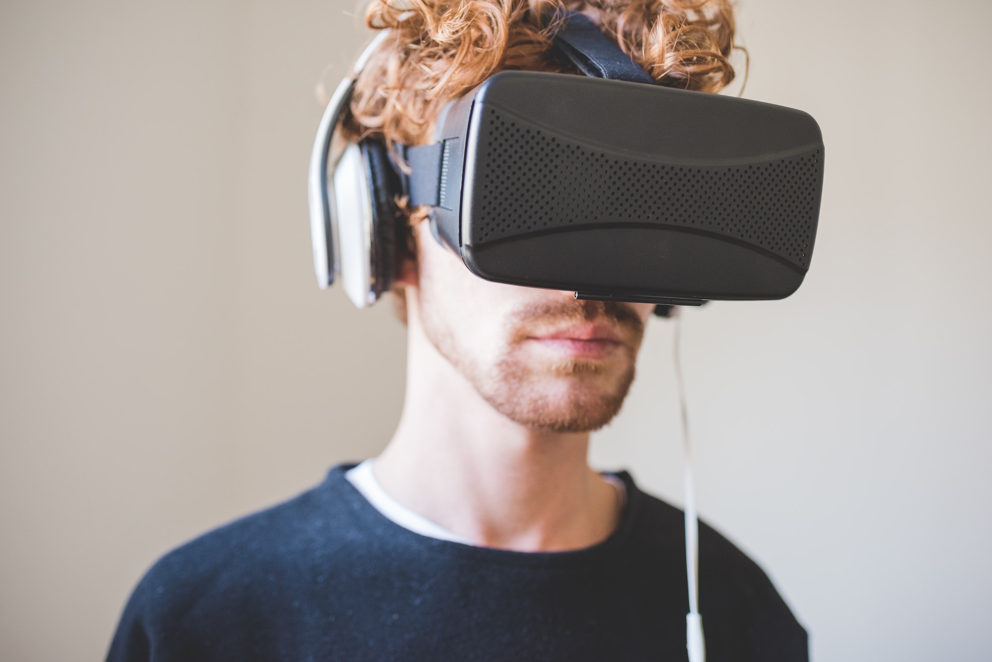 Young redhead man using 3D goggles wearing wireless headphones exploring metaverse